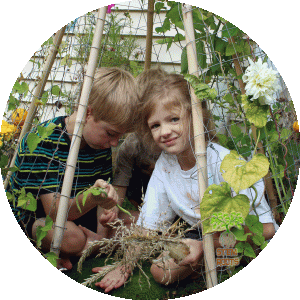 My kids showing off our Three Sisters crops from within our companion-planted teepee trellis. (The trellis included miniature pumpkins, Morning Glories, and beans.)